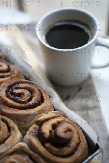 Freshly baked cinnamon rolls on a wooden board with a cup of coffee
