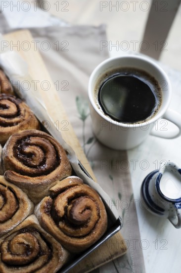 Freshly baked cinnamon rolls on a wooden board with a small pot of milk and a cup of coffee