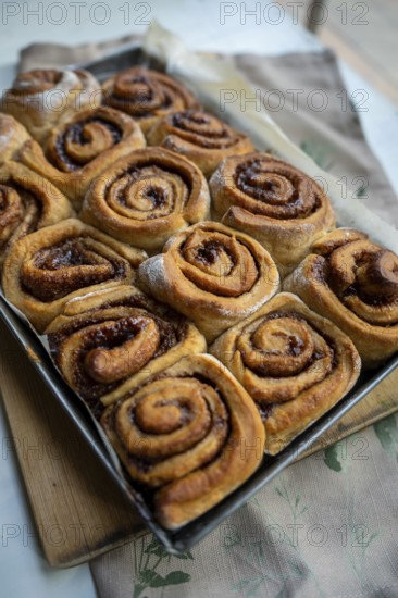 Freshly baked cinnamon roll on a wooden board with a small pot of milk