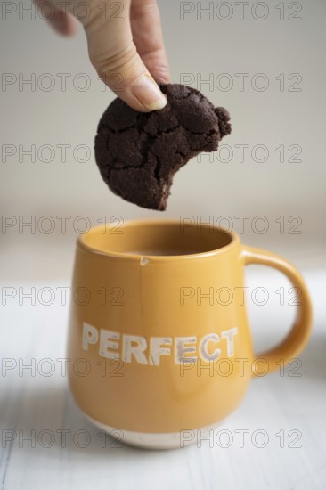 Chocolate chip cookie held over a cup of coffee with the imprint Perfect