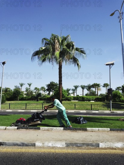 A local Egyptian man works on the infrastructure of a street in the resort town of Sharm el-Sheikh, mowing the grass with a lawnmower. South Sinai, Sharm el-Sheikh, Egypt