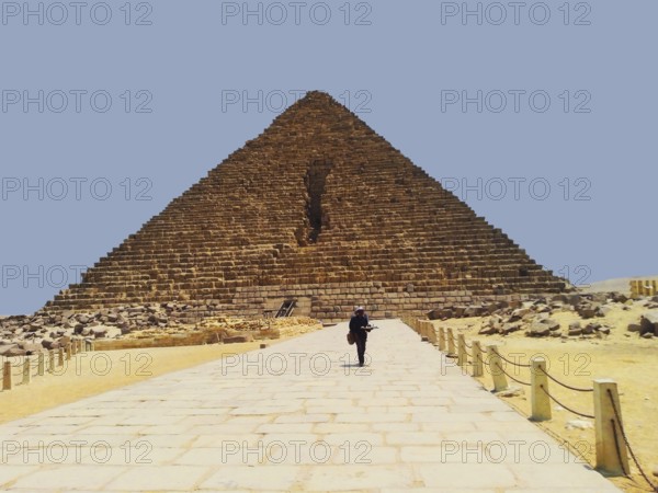 The majestic Pyramid of Menkaure, nestled in the sands of the African Sahara Desert, features a necropolis. One of the Seven Wonders of the Ancient Egyptian World, located on the Giza Plateau. A local souvenir vendor strolls along a stone alley. This architectural landmark attracts tourists and travelers from around the world. Middle East. Cairo, Egypt