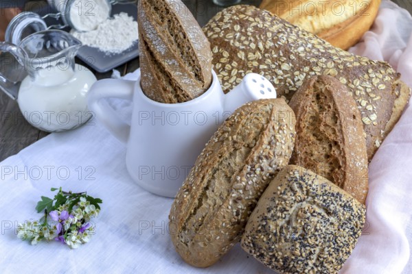 Freshly baked artisanal bread assortment, including baguettes, rolls, and loaves, with flour and milk on a wooden table