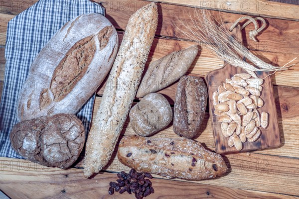 Freshly baked artisanal bread loaves, baguettes, and rolls on a wooden surface with wheat ears and raisins, symbolizing bakery craft