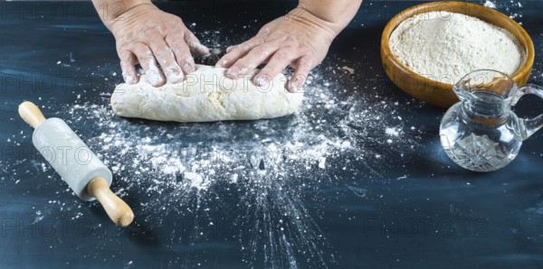Baker's hands carefully kneading uncooked dough on a dark kitchen counter, preparing traditional artisanal bread