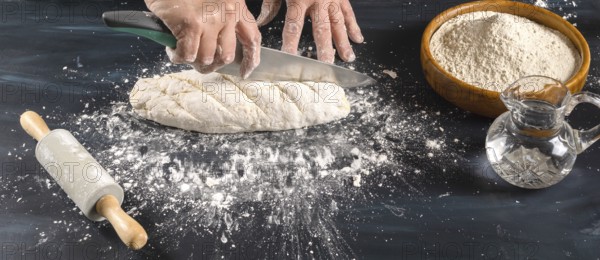 Hands of a baker scoring raw bread dough with a knife on a flour-dusted surface, preparing fresh homemade pastries