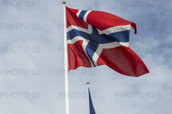 The national flag of Norway fluttering against the blue sky and gentle clouds. Oslo, Østlandet, Norway