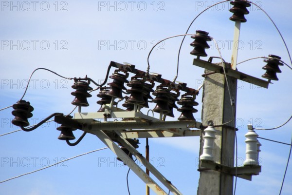 Electrical cables and ceramic, porcelain insulators of high voltage transmission line on top of concrete pole on the cloudscape background