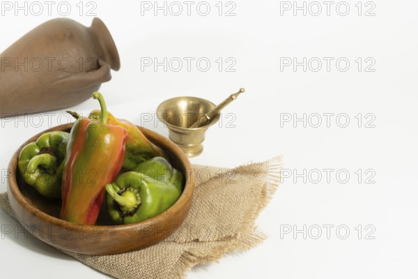 Green and red peppers in a wooden bowl on a white background, harvested from organic garden with copy-space