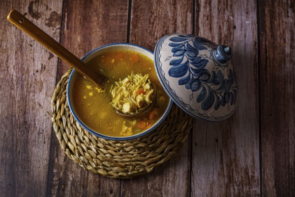 White and blue soup tureen with chicken noodle and vegetable soup with a wooden spoon