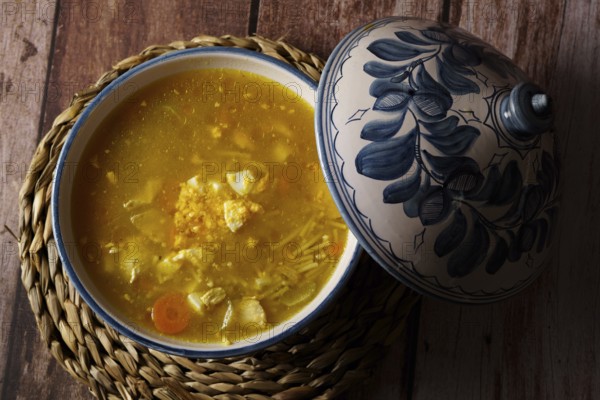 White and blue soup tureen with chicken noodle soup and vegetables with the lid open