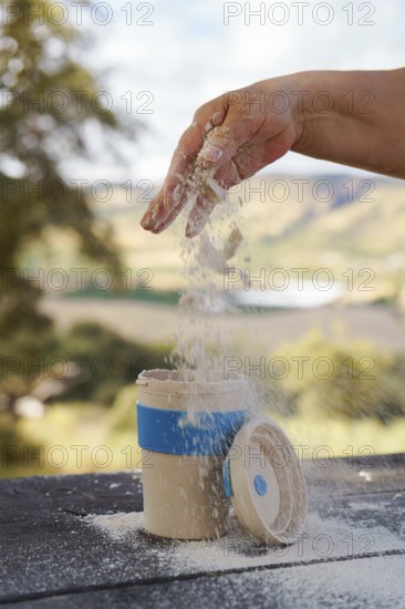 Hand pouring white powder from hand into a reusable portable mug on a wooden table, enjoying outdoor cooking
