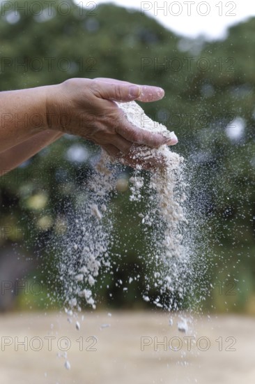 Hands holding and sifting white flour, with particles falling through fingers, demonstrating baking preparation