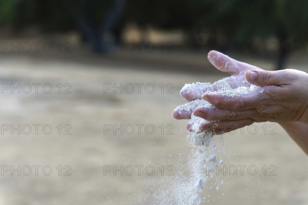 Hands releasing loose sand, grains falling through aged fingers to symbolize time, fragility, impermanence, and letting go