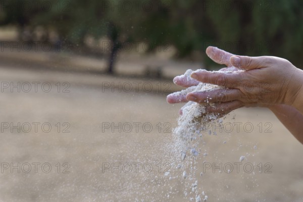 Hands pouring white sand, symbolizing the passage of time, impermanence, and the fleeting moments of life