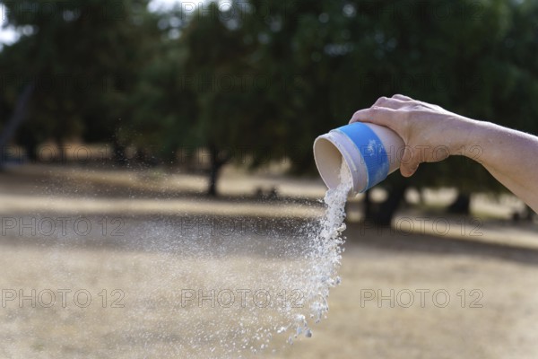 Hand pouring white chalk powder from a container, creating a cloud of dust dispersing in an outdoor setting