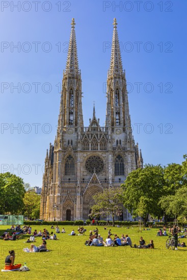 Young people enjoy the spring sun on the meadow in front of the neo-gothic votive church, Vienna, Austria