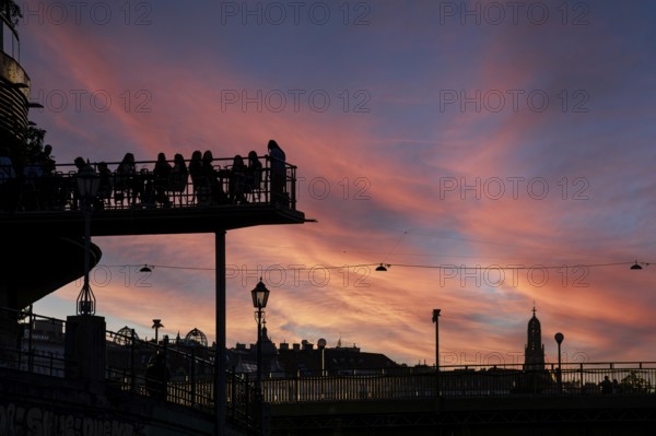 Visitors sit at sunset on the terrace of a cafe in the Urania am Danube Canal, Urania Observatory, Vienna, Austria
