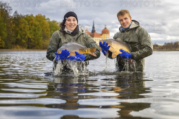Fish and forest festival. Marieluise Greitner and Kevin Kreutz from Teichwirtschaft Moritzburg keep carp in the for a photo opportunity while fishing the Moritzburg Castle Pond, Moritzburg, Saxony, Germany