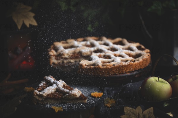 Icing sugar falls on apple pie surrounded by autumn leaves in a dark environment