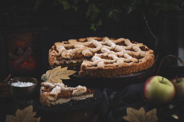 Sliced apple pie surrounded by autumn leaves in a dark environment