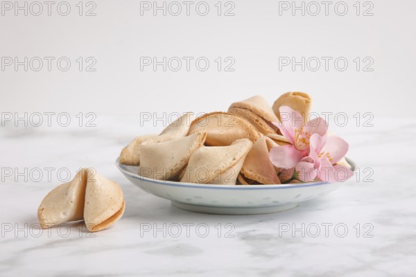 Fortune cookies in a Chinese bowl with a pink flower against a white background
