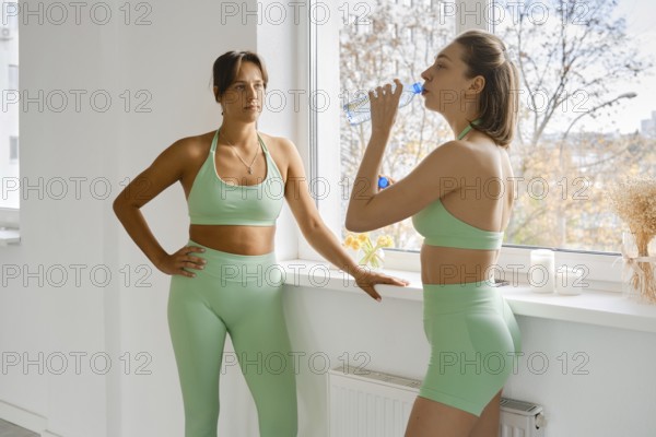 Break during fitness stretching class in bright studio with two women in green athletic wear