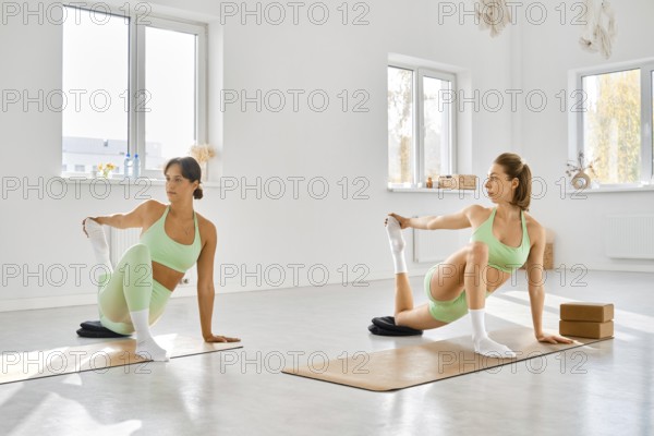 Two women practicing yoga stretches in a bright studio with natural light during daytime