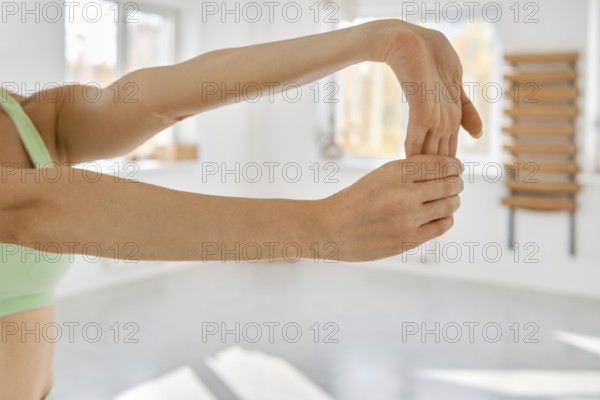 A person is performing a wrist stretch in a well-lit fitness studio. The individual extends their arm and gently pulls their fingers back to enhance flexibility