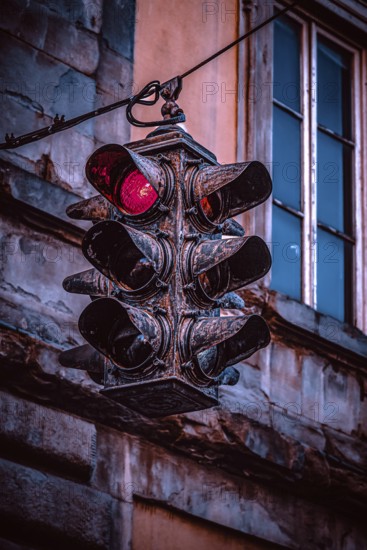 An old, weathered traffic light hangs in front of a building façade, shows red