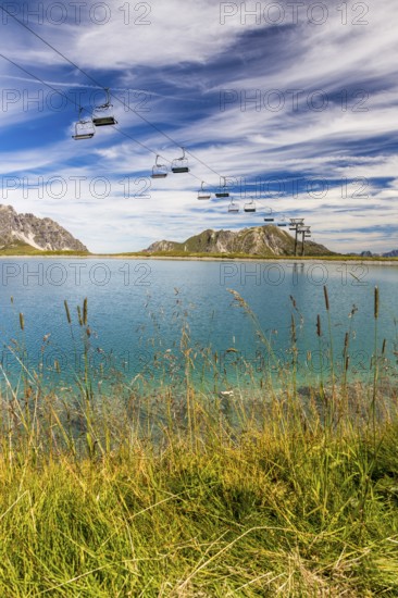 The panoramic lake on Saloberkopf with cable car and mountains in the background under a blue sky, Wart, Bregenz, Vorarlberg, Austria, Europe. A cable car leads across a lake in a mountainous landscape