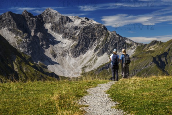 Two hikers stand in front of an impressive mountain backdrop under clear skies, Schröcken, Austria