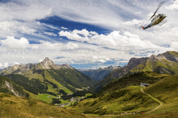 A helicopter flies over a mountainous landscape with blue skies and clouds