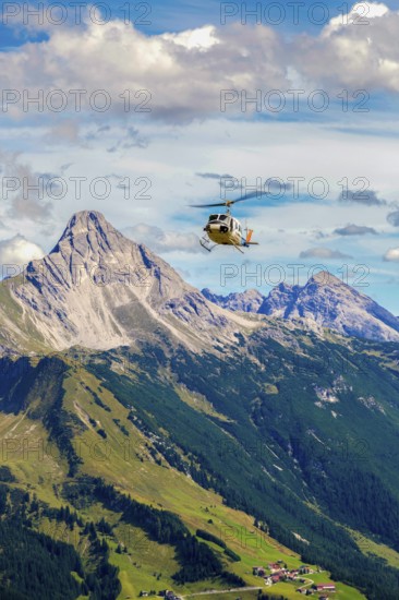 A helicopter flies over a mountainous region under a cloudy sky