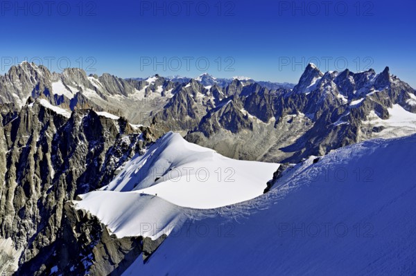Mountaineers climb over a snow-covered ridge with Grandes Jorasses mountain in the background, Aiguille du Midi mountain station, Chamonix-Mont-Blanc, Haute-Savoie, France