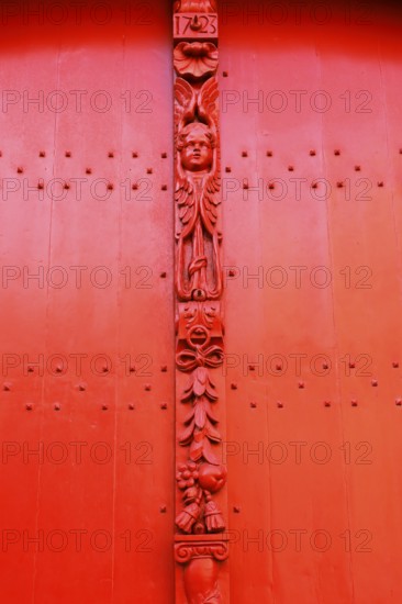 Red wooden door with decorative carvings and an angel figure at the entrance to the historic St. Salvator Cathedral, Sint-Salvatorskathedraal, in the old town of Bruges, UNESCO World Heritage Site, Flanders, Belgium