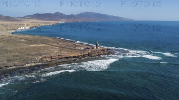 Aerial view of in the center lighthouse Faro Punta de Jandia at the southern tip of Jandia Peninsula, in the foreground white foam crowns on moving sea swell large high waves on reef edge, strong surf, Fuerteventura, Canary Islands, Canary Islands, Spain