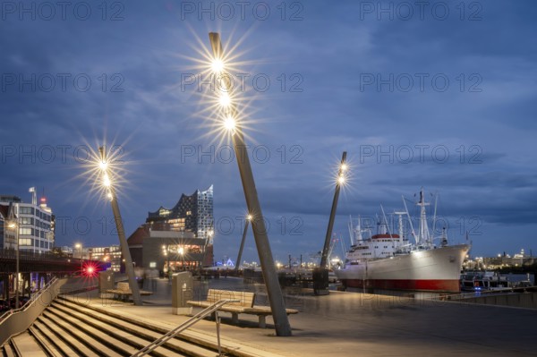 Blue hour at Hamburg Landungsbrücken with Elbe Philharmonic Hall, Cap San Diego ship and shining lanterns in the foreground, Hamburg, Germany