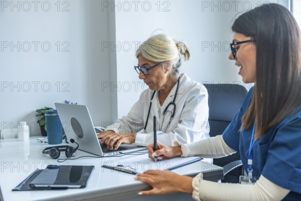 Two medical professionals, a senior doctor typing on a laptop and a younger nurse taking notes on a clipboard, are collaborating in a modern healthcare office environment