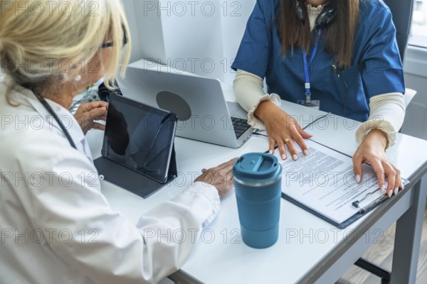 Healthcare team reviewing digital tablet and medical records, discussing patient care plans and data in a modern clinic setting, collaborating on diagnosis and treatment decisions