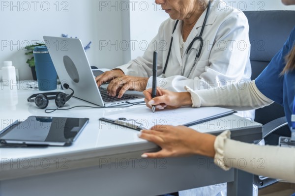 Medical team composed of a doctor and a nurse working together on patient files, with one typing on a laptop and the other writing notes, demonstrating teamwork in a modern healthcare setting