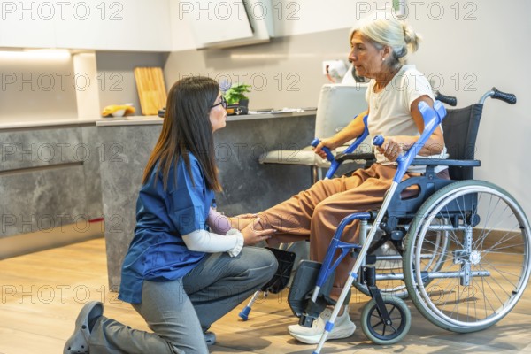 Nurse assisting an elderly woman in a wheelchair with home physiotherapy, providing gentle physical rehabilitation support to her leg and offering personal care indoors