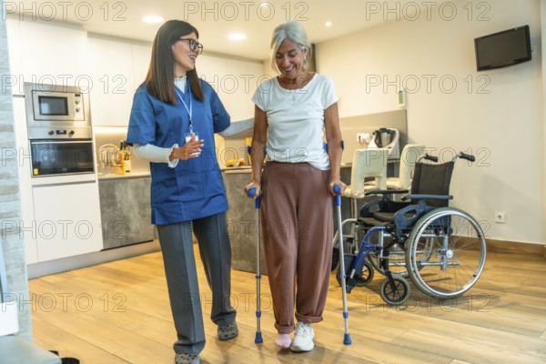 Young female nurse helping a happy elderly woman recovering from injury, walking with crutches during home care physiotherapy for rehabilitation and independent living