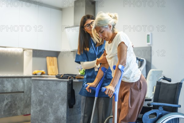 Young female caregiver is providing support and assistance to a senior woman, helping her during a home rehabilitation session, using a pair of crutches in a kitchen setting
