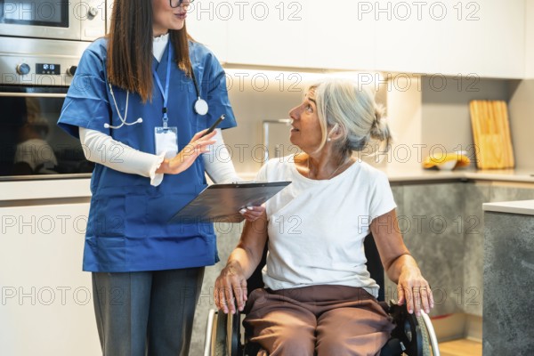 Nurse reviewing a healthcare plan with an elderly woman in a wheelchair in a modern kitchen, providing compassionate home care, support and guidance for independent living