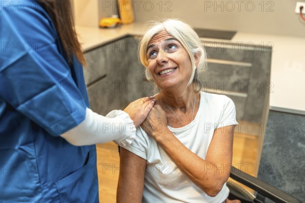 Healthcare professional in scrubs placing a comforting hand on the shoulder of a smiling senior woman with grey hair, illustrating elderly support and compassionate care in a home setting