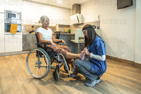 Physiotherapist in uniform giving gentle foot massage and rehabilitation treatment to a smiling senior woman in a wheelchair at home, promoting elderly care and recovery and comfort