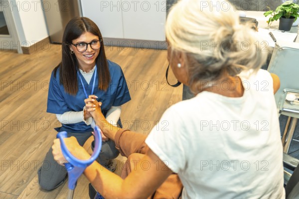 Happy young nurse providing professional foot physical therapy and care to an elderly woman using crutches, focusing on rehabilitation and home healthcare assistance
