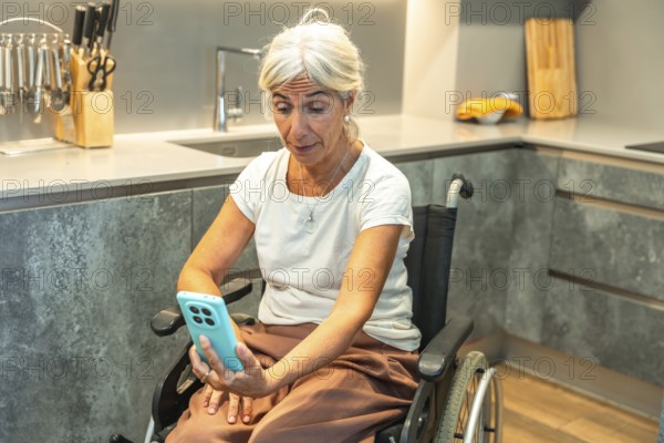 Senior woman in a wheelchair video calling on a smartphone from a modern kitchen, engaging in telehealth and social connection while demonstrating independence and everyday living
