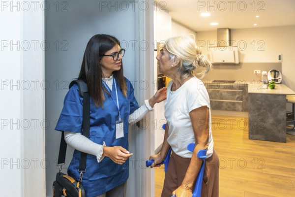 Caregiver wearing scrubs and carrying a medical bag assisting an elderly woman using crutches at the entrance of her brightly lit home, providing personal healthcare support
